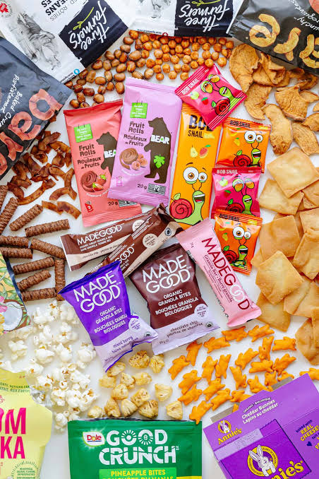Assorted healthy snack foods — granola bars, fruit rolls, roasted beans, and crackers on a white background